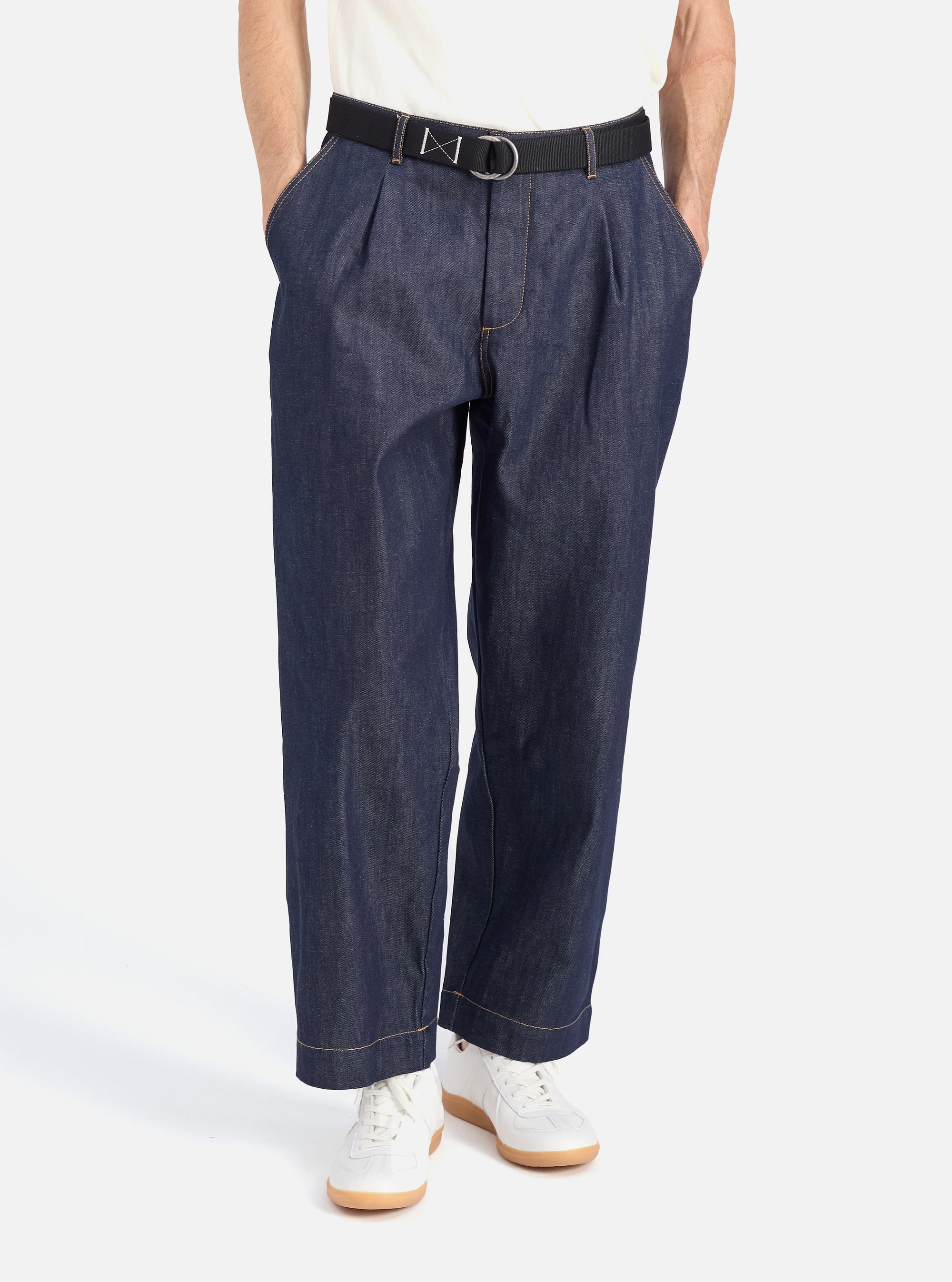 A model poses in the Indigo 13oz Selvedge Denim Duke Pant. The dark wash denim pants are styled with a black belt and white sneakers against a clean white background.