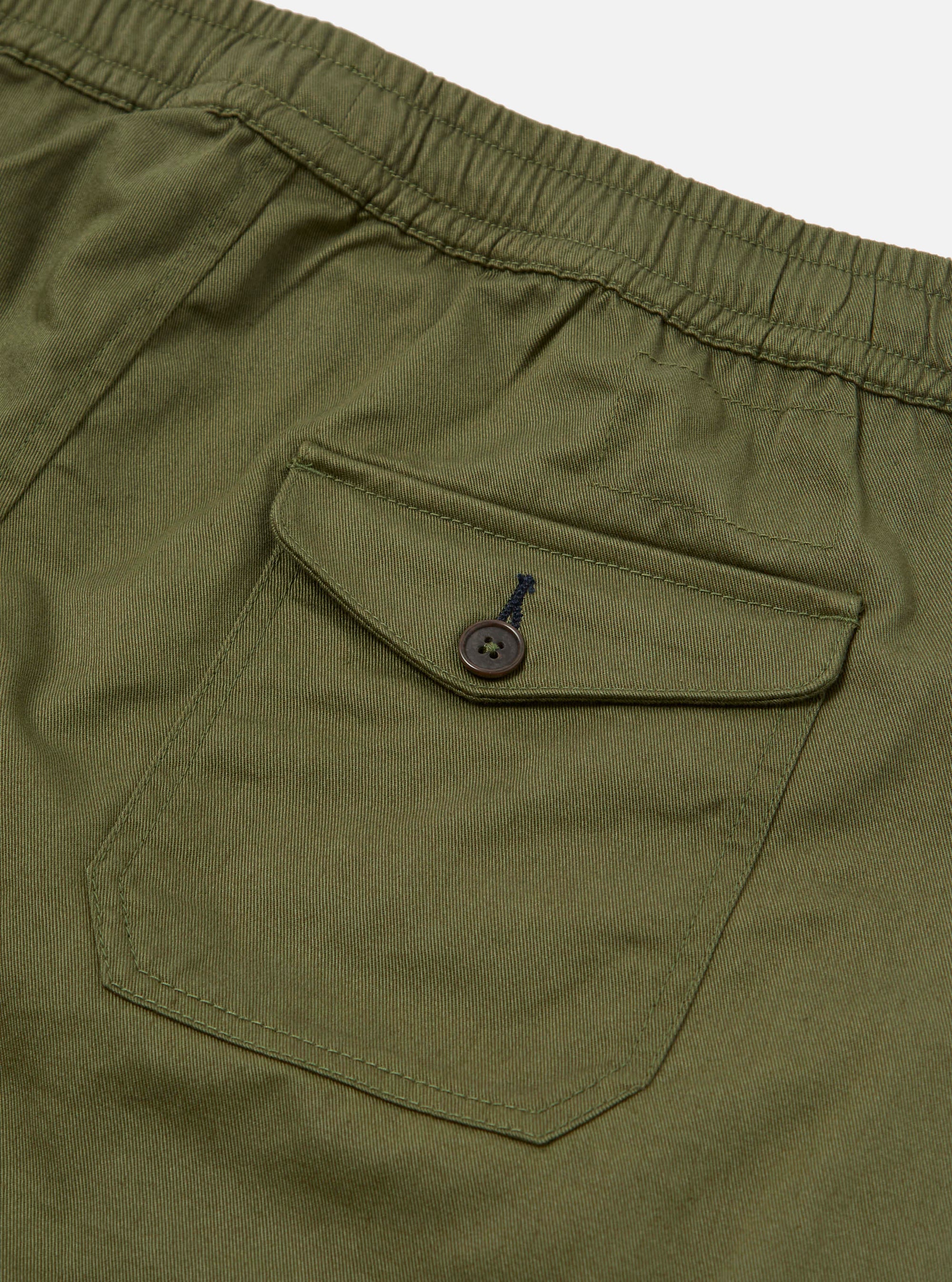 The Light Olive Twill Beach Short is shown from the back in a studio shot against a white background. The image highlights the single rear patch pocket with a visible eyelet and the elasticated waistband. The shorts are displayed as a flat lay with no model or mannequin present.
