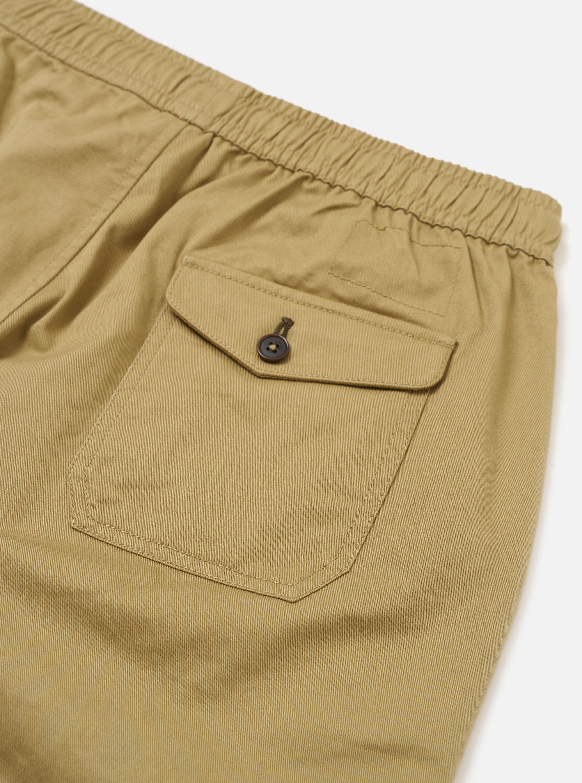 The Sand Twill Beach Short is displayed as a flat lay against a plain white background, showing the back of the garment. The shorts feature an elasticated waistband and a single patch pocket on the right rear side. The cotton twill fabric is a light sand color with a visible diagonal weave.