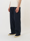 A model is wearing the Navy Twill Oxford Pant against a plain white background. The navy blue trousers feature a relaxed fit with a wide leg, a single pleat at the front, and a drawstring at the elasticated waistband. The model is also wearing a light-colored shirt and white sneakers.