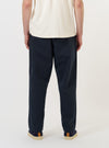 A model is wearing the Navy Twill Oxford Pant against a plain white background. The image provides a close-up view from the waist down, showcasing the dark navy fabric, a pleated front, and side pockets. The trousers have a loose, wide-leg fit.