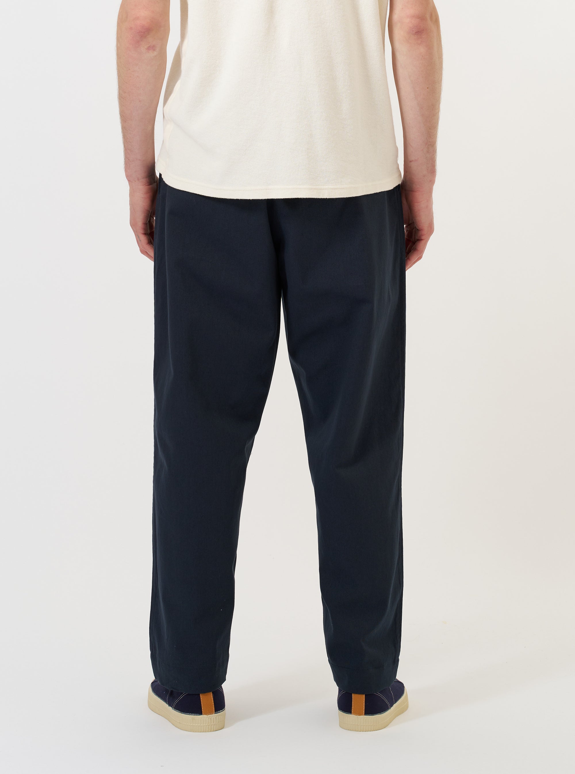 A model is wearing the Navy Twill Oxford Pant against a plain white background. The image provides a close-up view from the waist down, showcasing the dark navy fabric, a pleated front, and side pockets. The trousers have a loose, wide-leg fit.