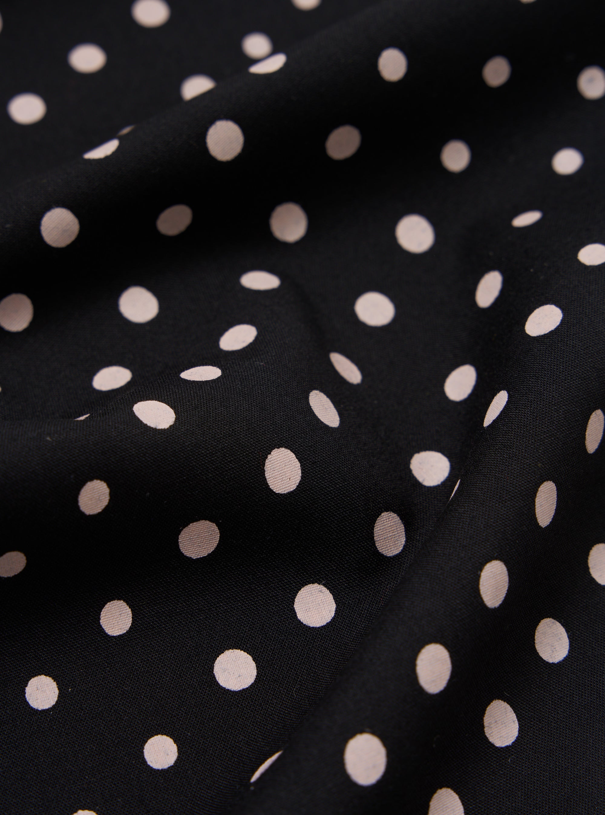 Close-up of a draped Black Dot Print Short Scarf. The scarf has a black background with small, light pink polka dots. The fabric is softly folded.