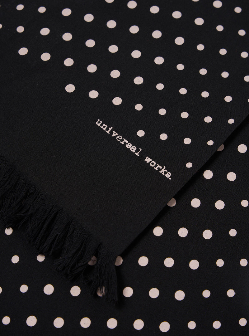 Close-up of a Black Dot Print Short Scarf with fringe. The scarf has white dots and the words "universal works."