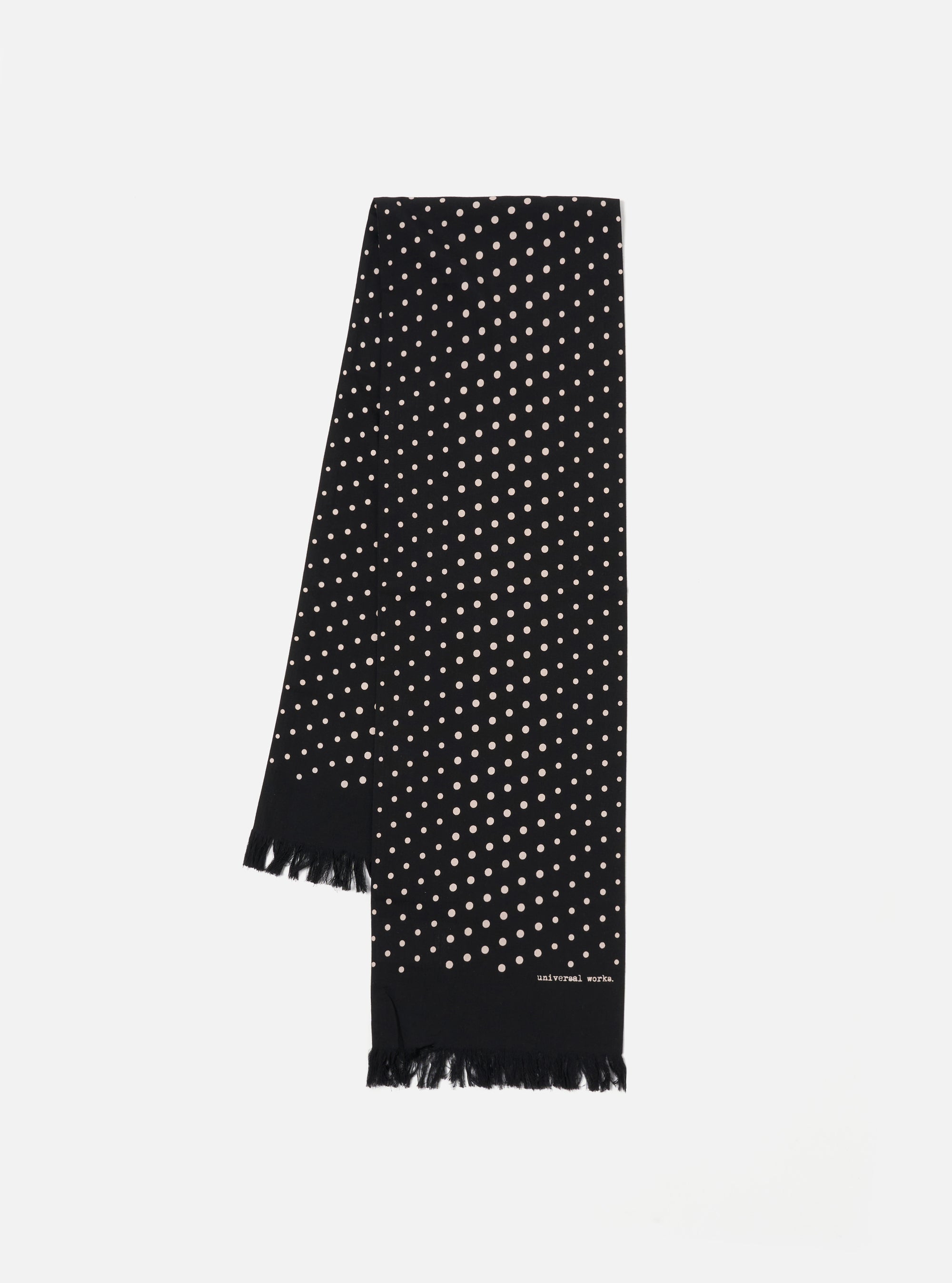 Draped on a white surface, a Black Dot Print Short Scarf. The black scarf features small white dots and a fringed edge. The brand name is printed near the bottom.