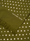Close-up of a Green Dot Print Short Scarf. The olive green scarf has white polka dots and a fringed edge. The words "universal works." are printed on the fabric.