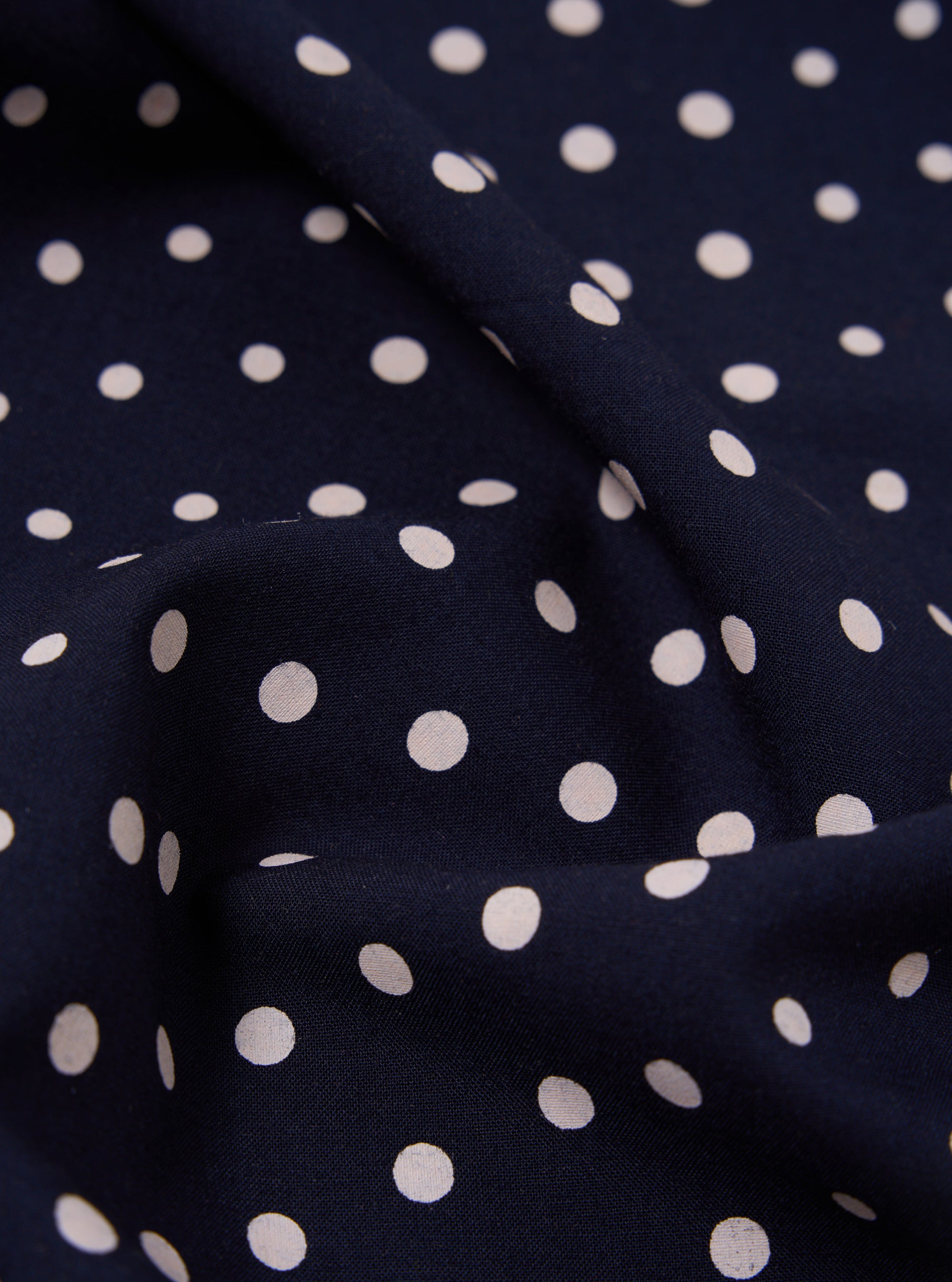 Close-up of a Navy Dot Print Short Scarf, showing the fabric's texture and pattern. The scarf is draped on a flat surface, highlighting the navy background and white polka dots.
