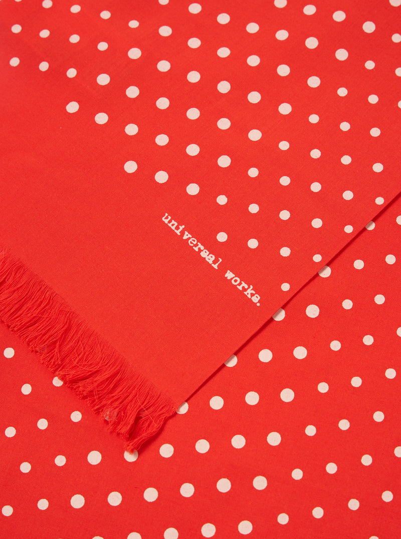 Close-up of an Orange Dot Print Short Scarf. The scarf is red with white polka dots and a fringed edge. The words 'universal works' are printed on the scarf.