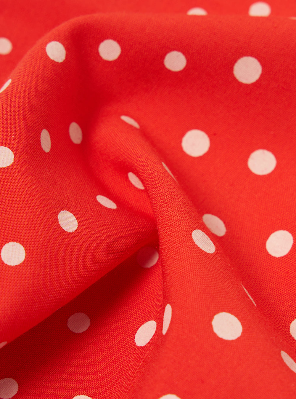 Close-up of an Orange Dot Print Short Scarf. The red fabric has white polka dots and is draped to show texture. 