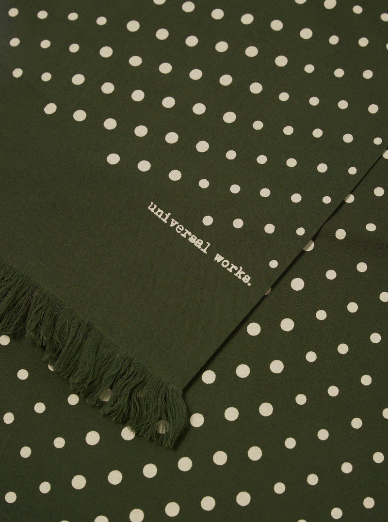 Close-up of the Olive Dot Print Short Scarf, featuring an olive green fabric with white polka dots and fringed edge. The words 'universal works.' are printed on the scarf.