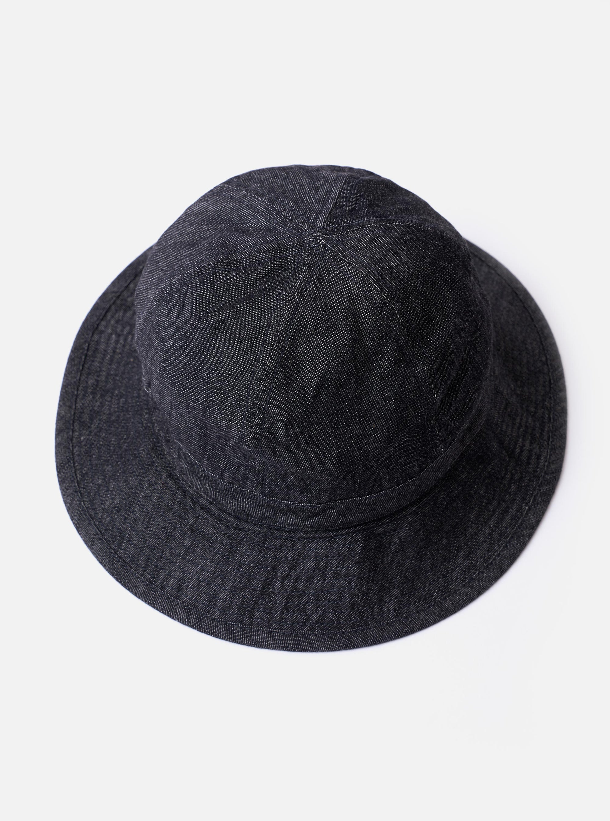 The cableami Black 10oz Denim Metro Hat is shown from a rear angle as a flat lay against a plain white background. The image highlights the rounded crown construction and the downward-sloping brim of the black denim fabric. A black adjustable drawcord with a plastic toggle and a detachable strap are visible.