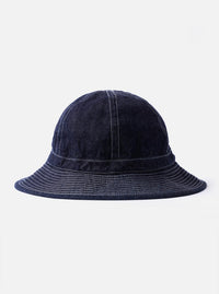 The cableami Indigo 10oz Denim Metro Hat is shown as a flat lay against a white background. The hat is made from a deep indigo blue denim and features a rounded crown, a downward-sloping brim with tonal topstitching, and an adjustable strap with a toggle.