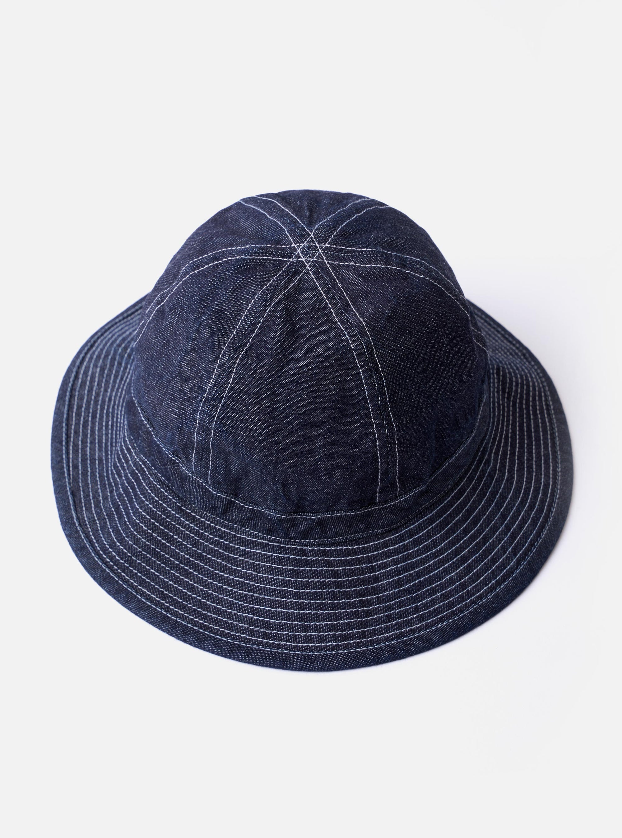 The cableami Indigo 10oz Denim Metro Hat is shown from a rear three-quarter angle as a flat lay against a plain white background. The image highlights the hat's rounded crown, downward-sloping brim with tonal stitching, and an adjustable strap cord featuring a plastic toggle.