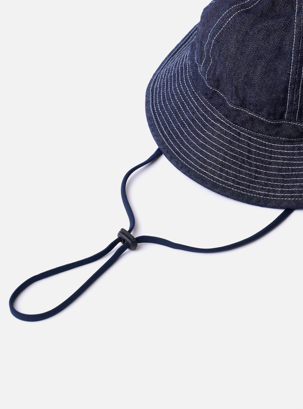 The cableami Indigo 10oz Denim Metro Hat is shown from a rear three-quarter angle as a flat lay against a plain white background. The image highlights the rounded crown and downward-sloping brim, as well as the adjustable drawcord and stopper at the back. The indigo denim fabric features a visible natural slub texture.