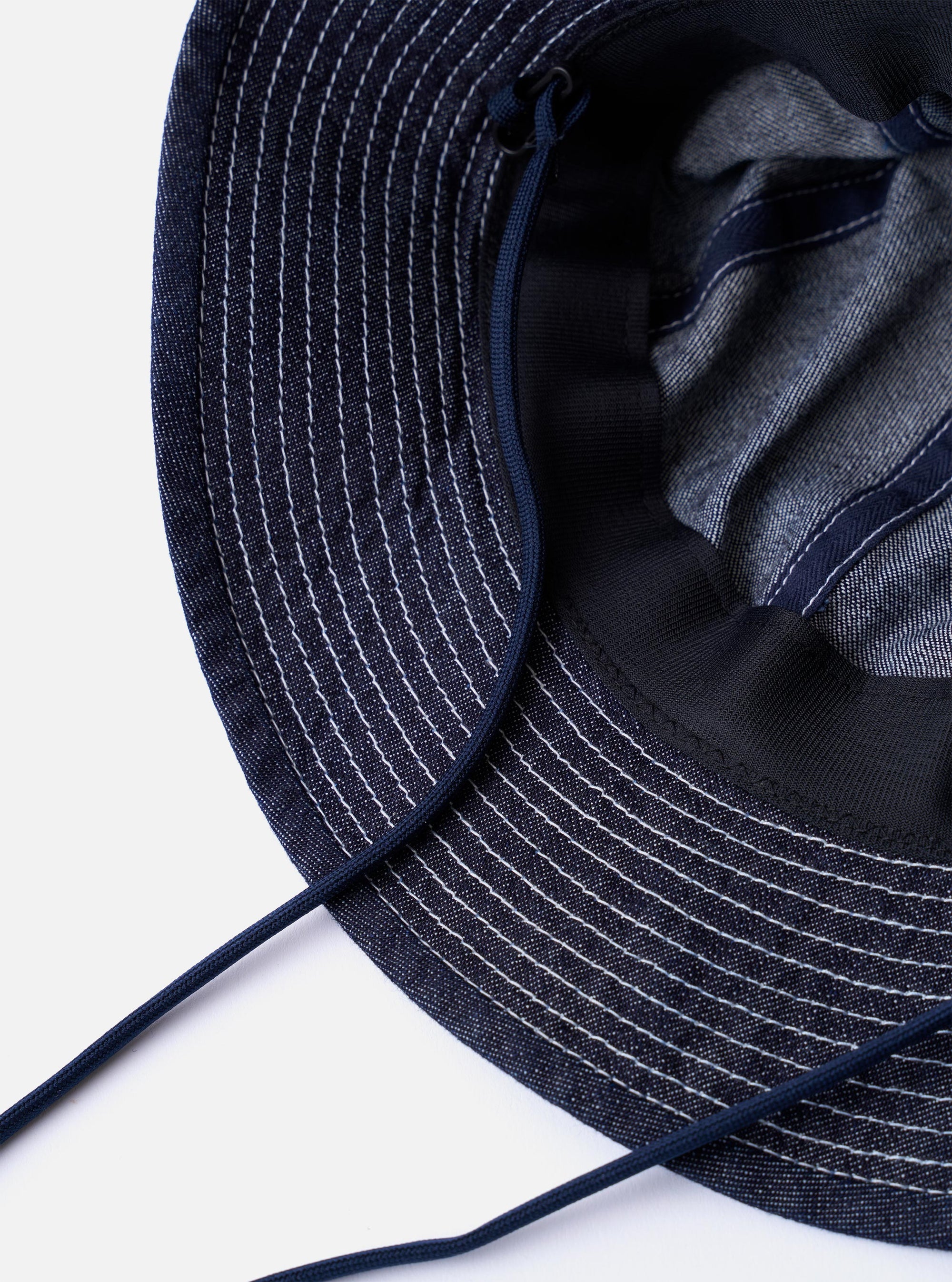 The cableami Indigo 10oz Denim Metro Hat is shown from the back as a flat lay against a plain white background. The image highlights the rounded crown construction, the stitching detail on the brim, and the adjustable toggle on the dark cord.