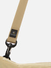 The master-piece x Universal Works Beige Canvas Sacoche is shown from a rear angle as a flat lay against a plain white background. The image highlights the clean back panel of the beige canvas bag, the black adjustable shoulder strap attached with metal hardware, and the black zippered rear pocket.