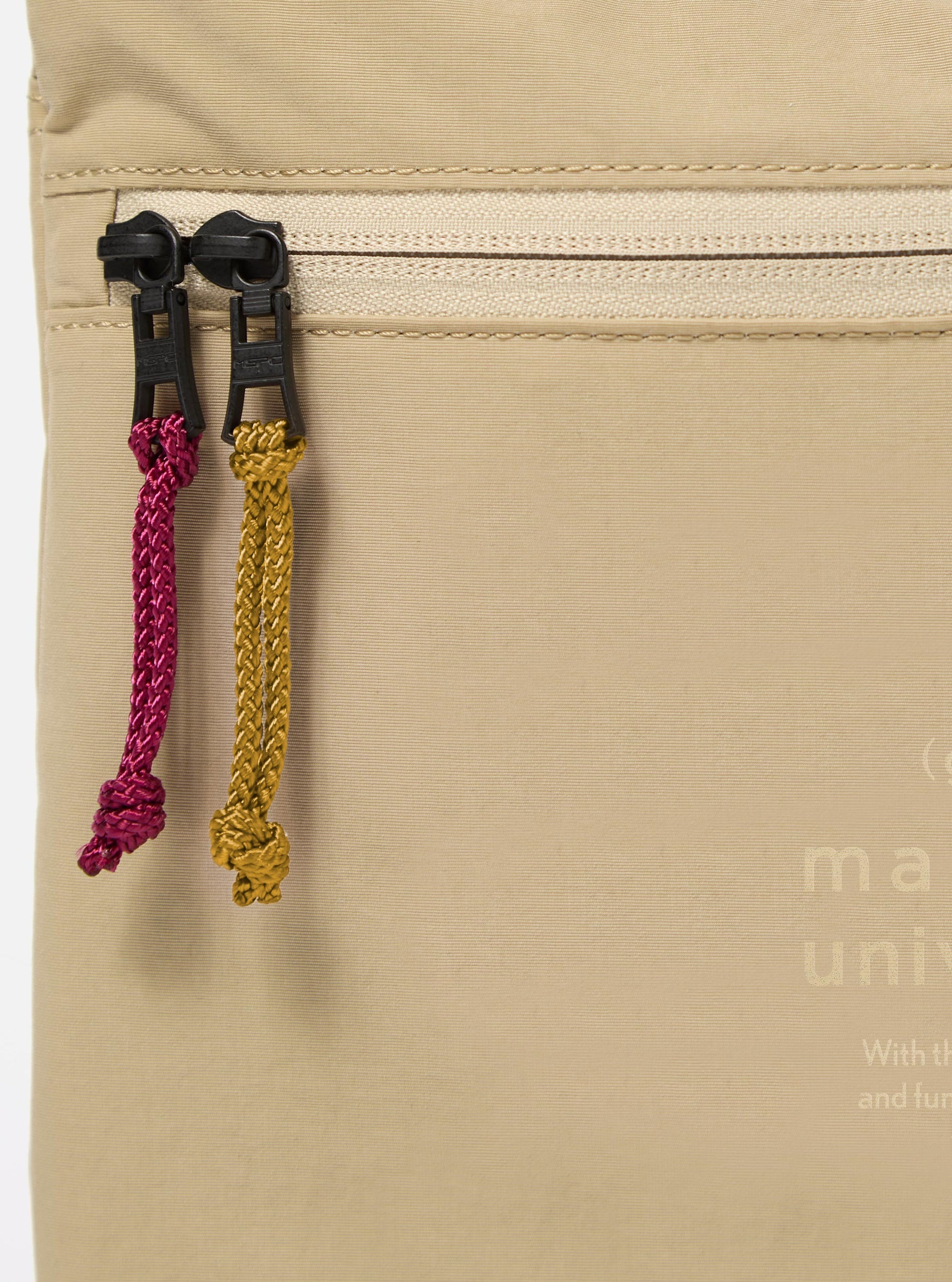 The master-piece x Universal Works Beige Canvas Sacoche is shown from a rear angle as a flat lay against a plain white background. The image highlights the adjustable and removable black crossbody strap attached with metal clips, the clean construction of the back panel, and the durable beige canvas fabric.
