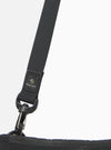 The master-piece x Universal Works Black Canvas Sacoche is shown from a rear three-quarter angle as a flat lay against a white background. The image highlights the adjustable black shoulder strap attached with metal clips, a rear slip pocket, and the durable texture of the black canvas fabric.