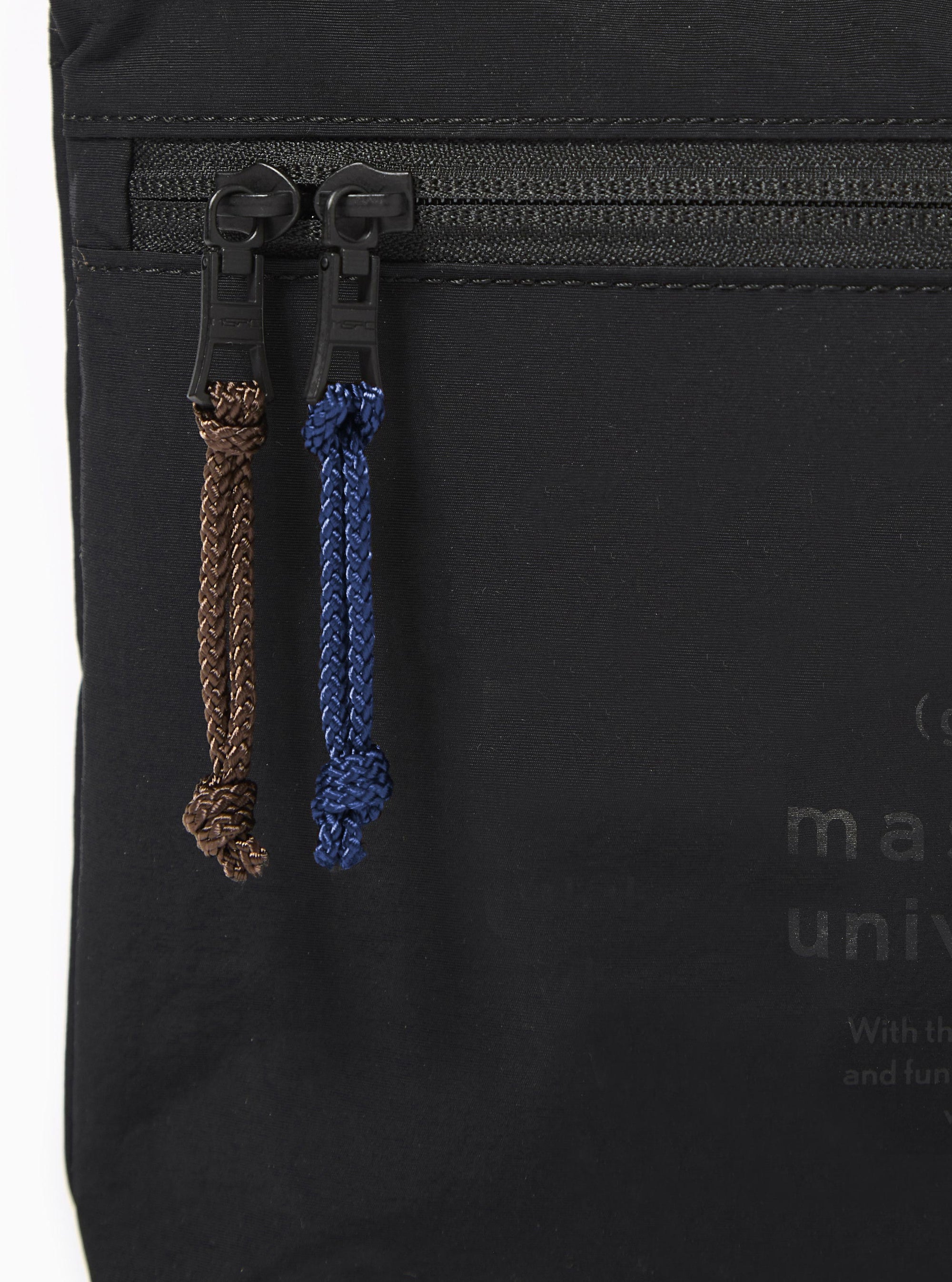 The master-piece x Universal Works Black Canvas Sacoche is displayed from a rear angle as a flat lay against a plain white background. The image highlights the adjustable black shoulder strap attached to the top corners and a small exterior pocket on the back panel. The black canvas fabric has a matte finish with visible tonal stitching.