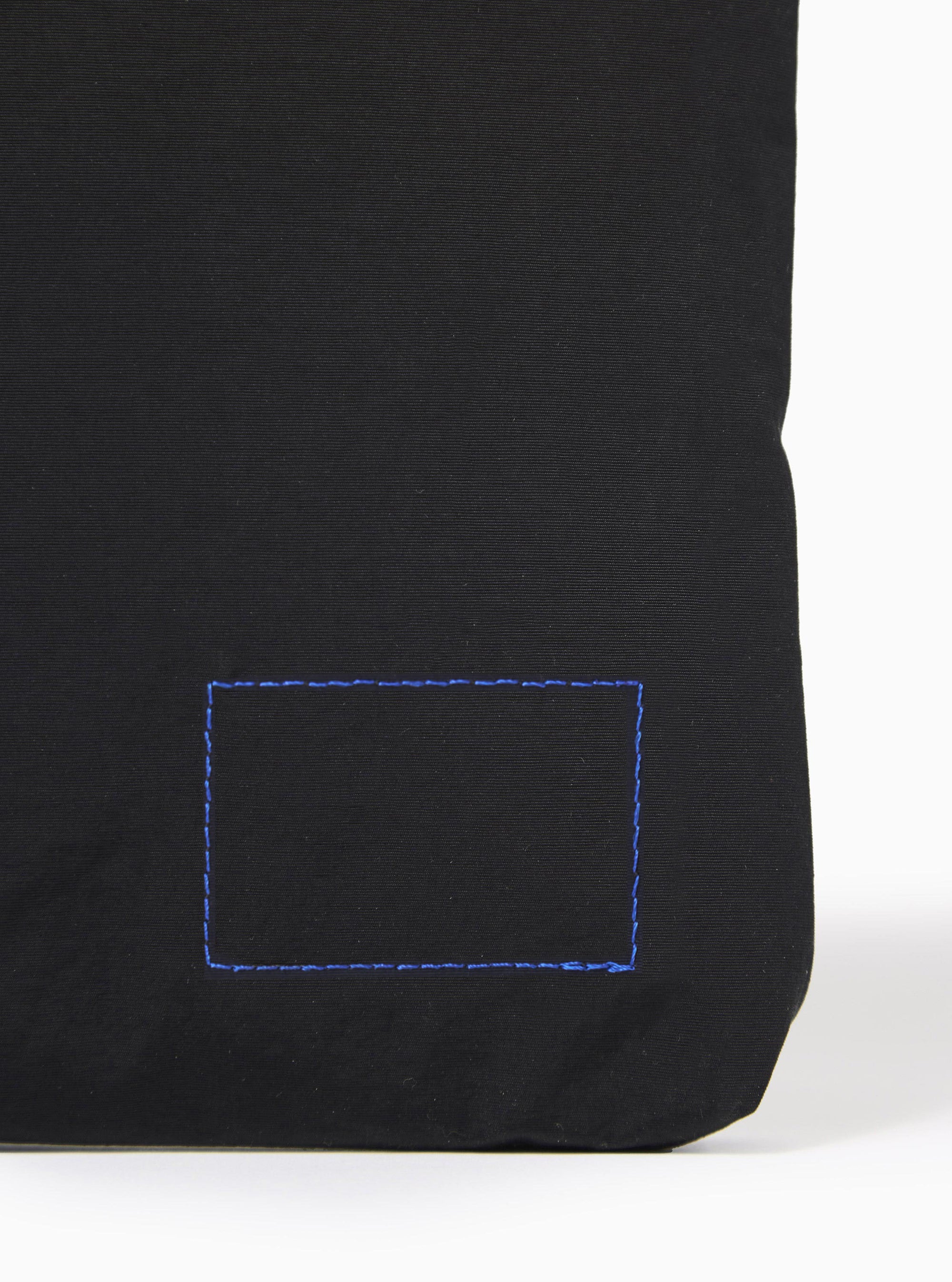 The master-piece x Universal Works Black Canvas Sacoche is shown in a detail view as a flat lay against a plain white background. The image focuses on the adjustable black shoulder strap and the metal hardware, including a swivel lobster clasp and a slider buckle. The durable black canvas fabric and clean stitching of the bag's attachment point are clearly visible.