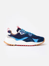 The Flower Mountain Navy/Azure Suede/Nylon Wave Man sneaker is shown from a side profile as a flat lay against a plain white background. The shoe features a technical fabric upper in navy blue with tonal suede overlays and light blue azure accents. It is designed with a classic lace-up system, flower-shaped eyelets, a webbing back pull tab, and a white rubber sole with a distinct notched edge.