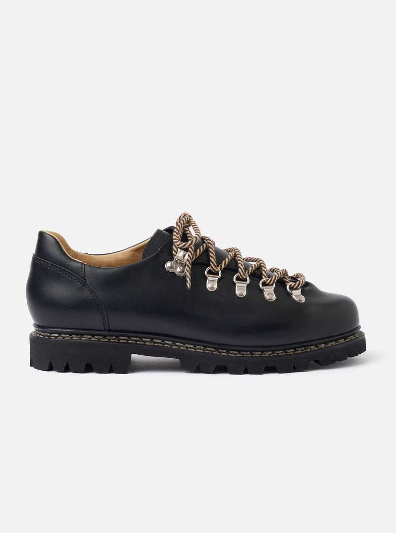 The Paraboot Black Leather Clusaz Jannu is shown from a side profile as a flat lay against a plain white background. The shoe is a low-cut hiking style made from smooth black leather with a prominent chunky rubber lug sole and visible Norwegian welt stitching. It features metal D-ring eyelets and black laces.