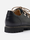 The Paraboot Black Leather Clusaz Jannu is shown from a rear three-quarter angle against a plain white background. The image highlights the shoe's low-cut hiking silhouette, featuring a chunky black rubber lug sole and a visible Norwegian welt construction. The smooth black leather upper, tonal stitching, and sturdy heel counter are clearly displayed.