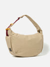 The master-piece x Universal Works Beige Large Canvas Shoulder Bag is shown from the back as a flat lay against a plain white background. The image highlights the bag's large, rectangular shape and the light beige canvas fabric. A single adjustable shoulder strap is attached, and a small black collaboration tag is visible on the lower right side.