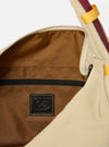 The master-piece x Universal Works Beige Large Canvas Shoulder Bag is shown from the back as a flat lay against a plain white background. The image highlights the wide, adjustable shoulder strap, a large external patch pocket with a dual-branded master-piece and Universal Works logo, and the durable beige canvas construction.