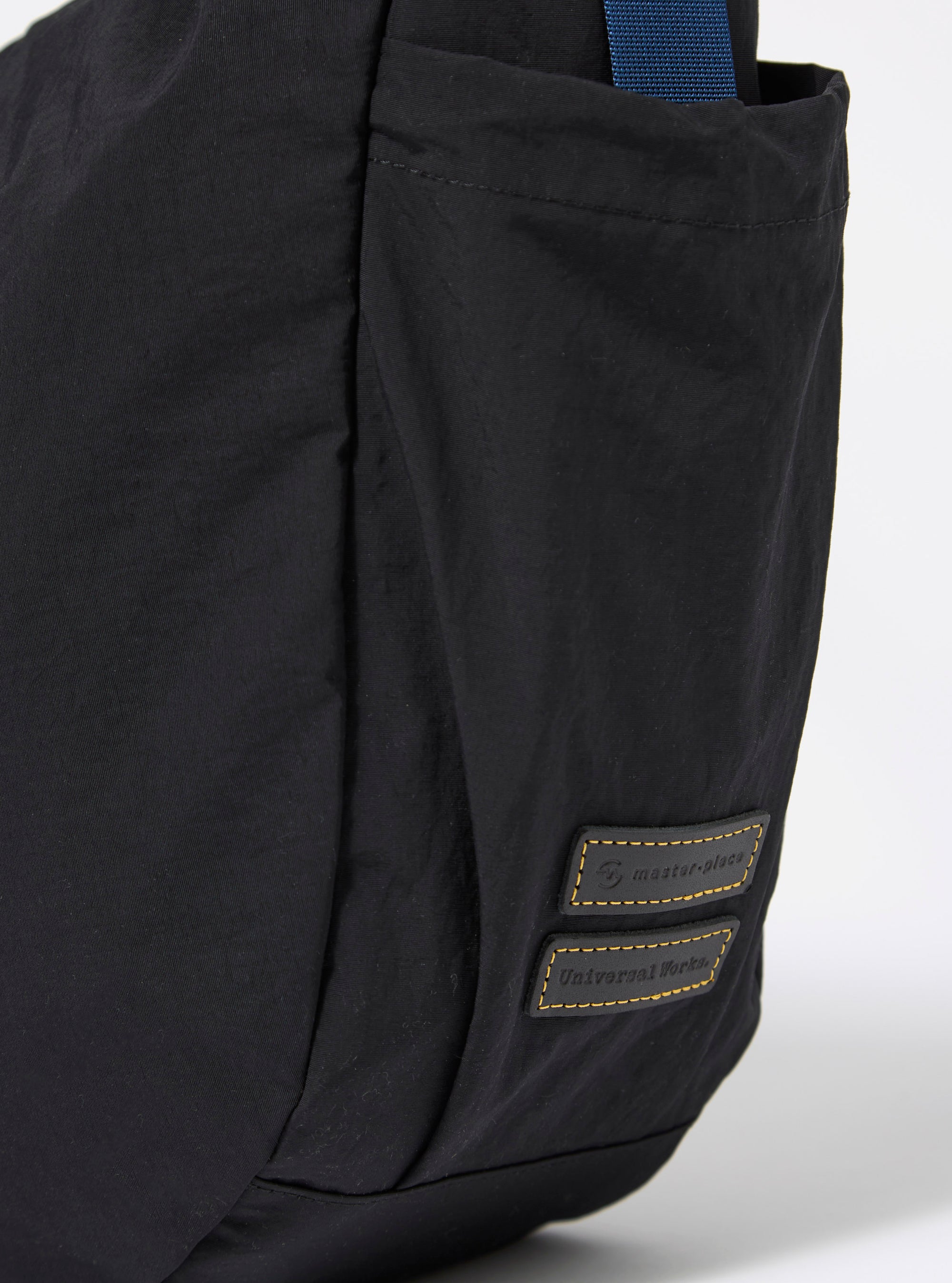 The master-piece x Universal Works Black Large Canvas Shoulder Bag is shown from the back as a flat lay against a plain white background. The image highlights the clean construction of the bag's rear, the black canvas material, and the adjustable black shoulder strap.
