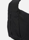 The master-piece x Universal Works Black Large Canvas Shoulder Bag is shown from the back as a flat lay against a plain white background. The image highlights the bag's durable black canvas construction, featuring a small woven brand tag near the bottom seam and clean tonal stitching throughout.