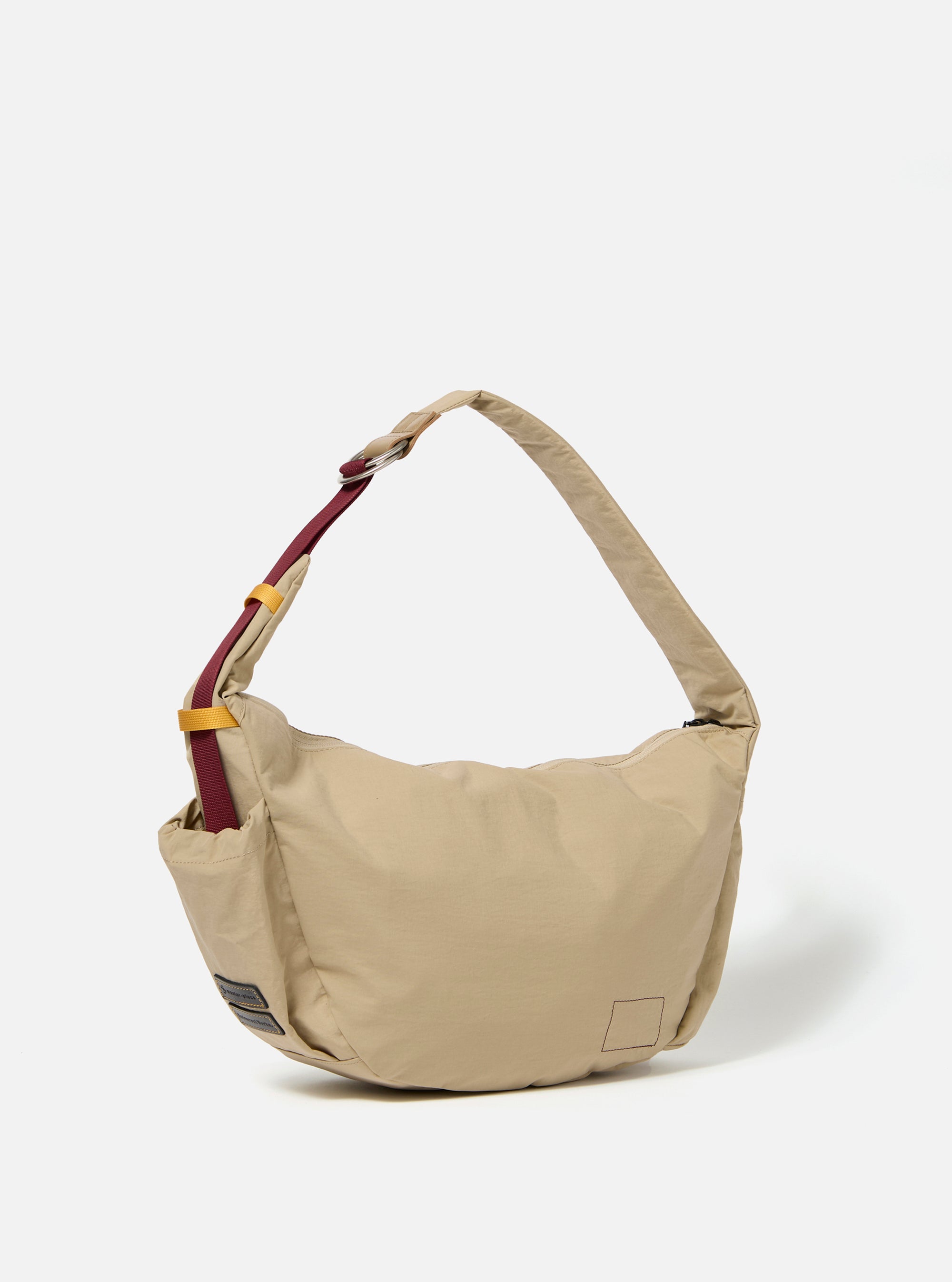 The master-piece x Universal Works Beige Medium Canvas Shoulder Bag is shown from the back as a flat lay against a plain white background. The image highlights the adjustable shoulder strap, a large rear compartment, and the durable beige canvas construction.