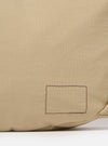 The master-piece x Universal Works Beige Medium Canvas Shoulder Bag is shown from a rear three-quarter angle as a flat lay against a plain white background. The image highlights the adjustable shoulder strap with its black plastic buckle and the clean, structured back panel of the beige canvas bag.