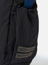 The master-piece x Universal Works Black Medium Canvas Shoulder Bag is shown from the back as a flat lay against a plain white background. The image highlights the clean, rectangular construction of the bag and the smooth texture of the black canvas fabric. A small black brand tag is visible on the side.