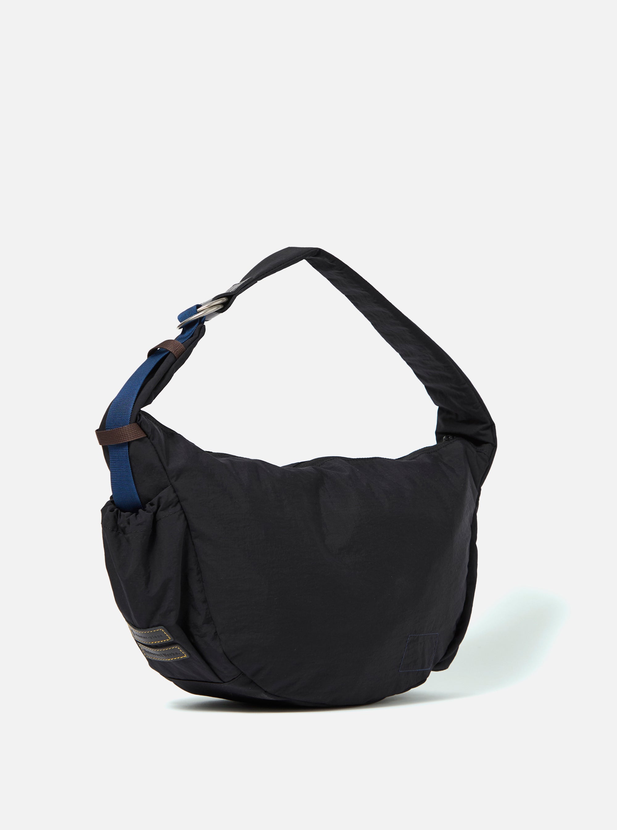 The master-piece x Universal Works Black Medium Canvas Shoulder Bag is shown from the back as a flat lay against a plain white background. The image highlights the adjustable black shoulder strap and the clean, rectangular construction of the bag's rear.