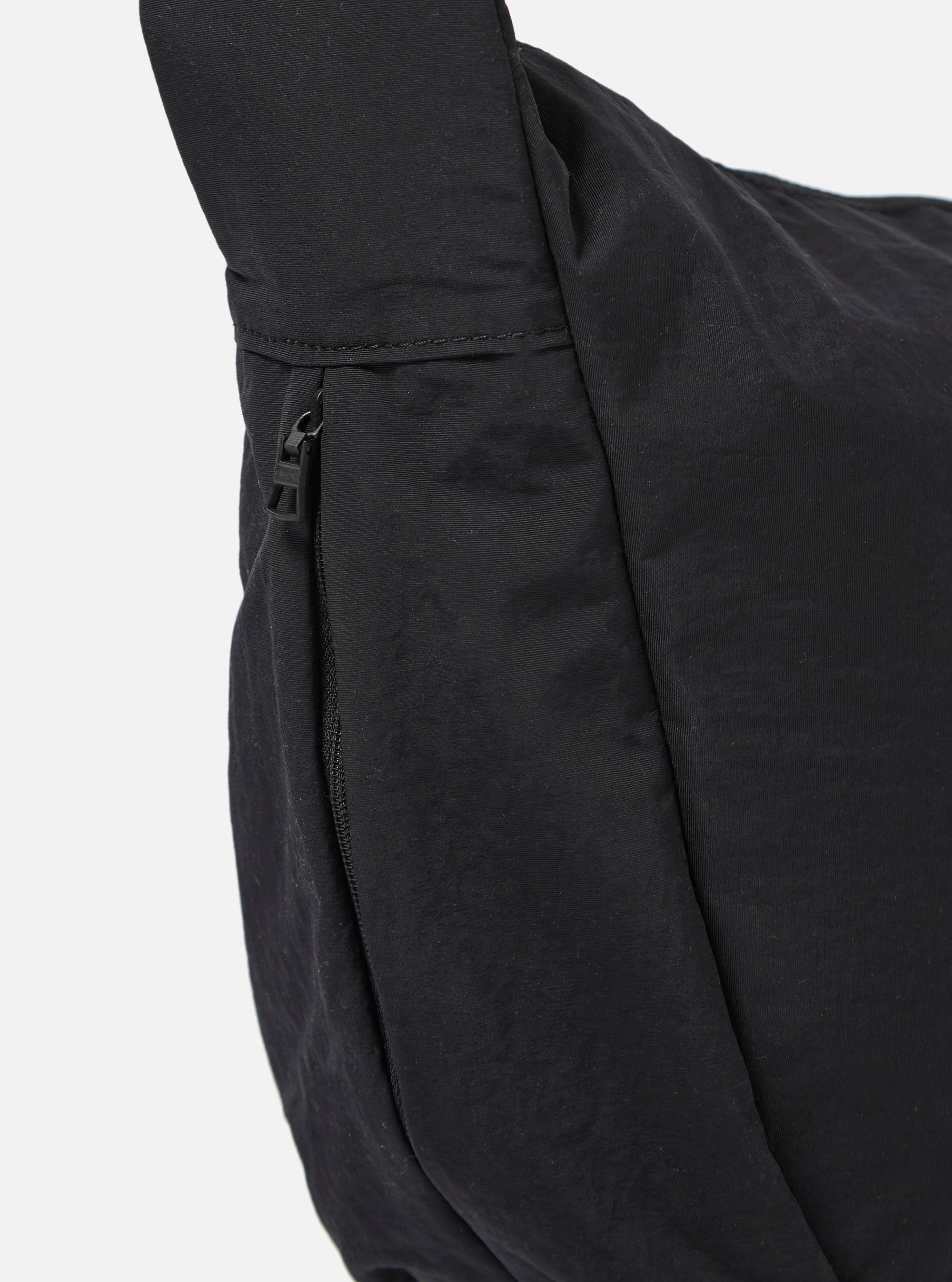The master-piece x Universal Works Black Medium Canvas Shoulder Bag is shown from the back as a flat lay against a plain white background. The image highlights the adjustable black webbing shoulder strap attached with metal hardware and the clean, rectangular construction of the bag's rear. The canvas fabric has a smooth, matte black finish.