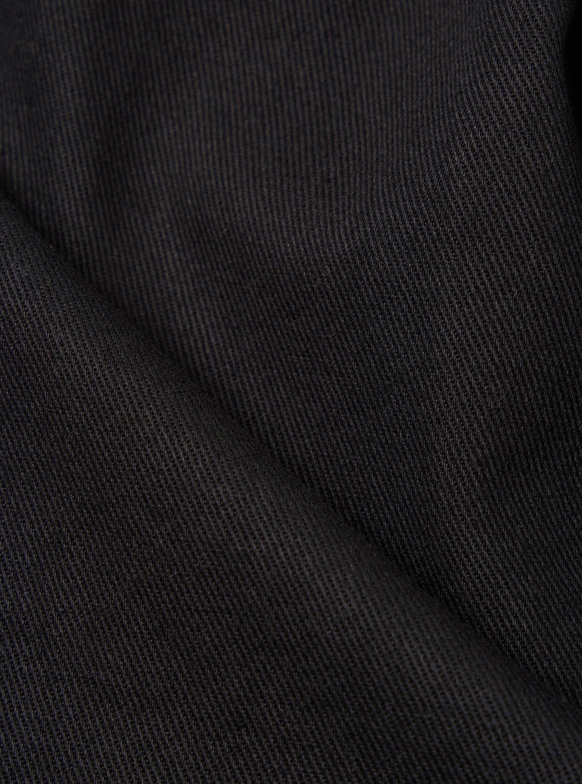 Close-up of Black Twill Military Chino fabric. The dark, textured material is neatly folded, showcasing its fine weave and durable construction. 