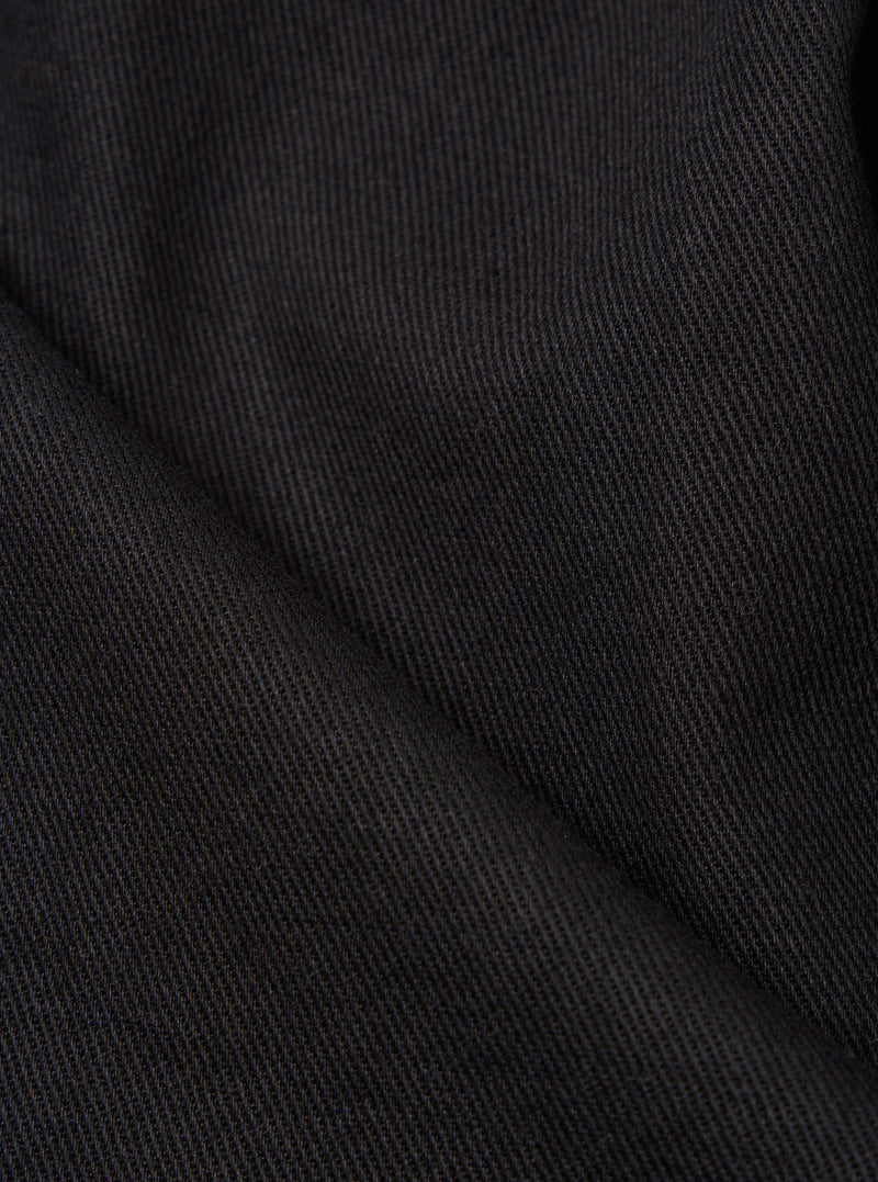 Close-up of the Black Twill Duke Pant fabric. The dark, textured twill is neatly folded on a plain surface, highlighting the material's weave.
