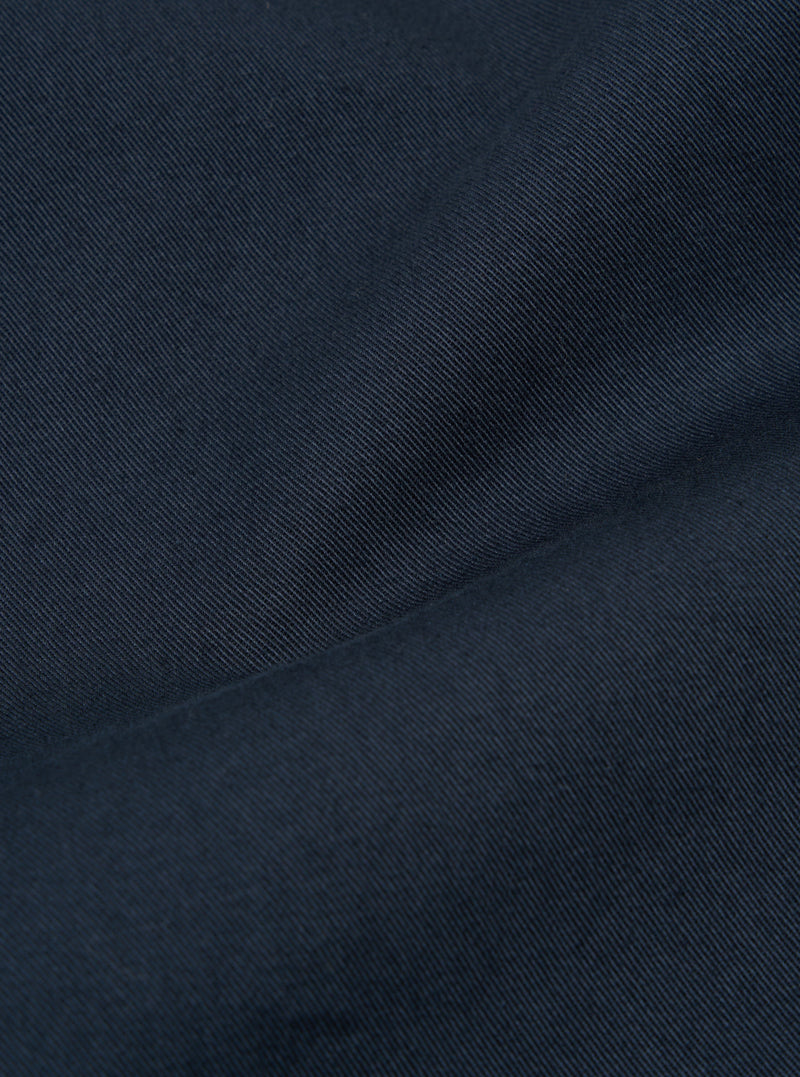 Close-up of the Navy Twill Fatigue Pant fabric. The twill weave is visible, showing the texture and color of the material. The pants are folded on a plain surface.