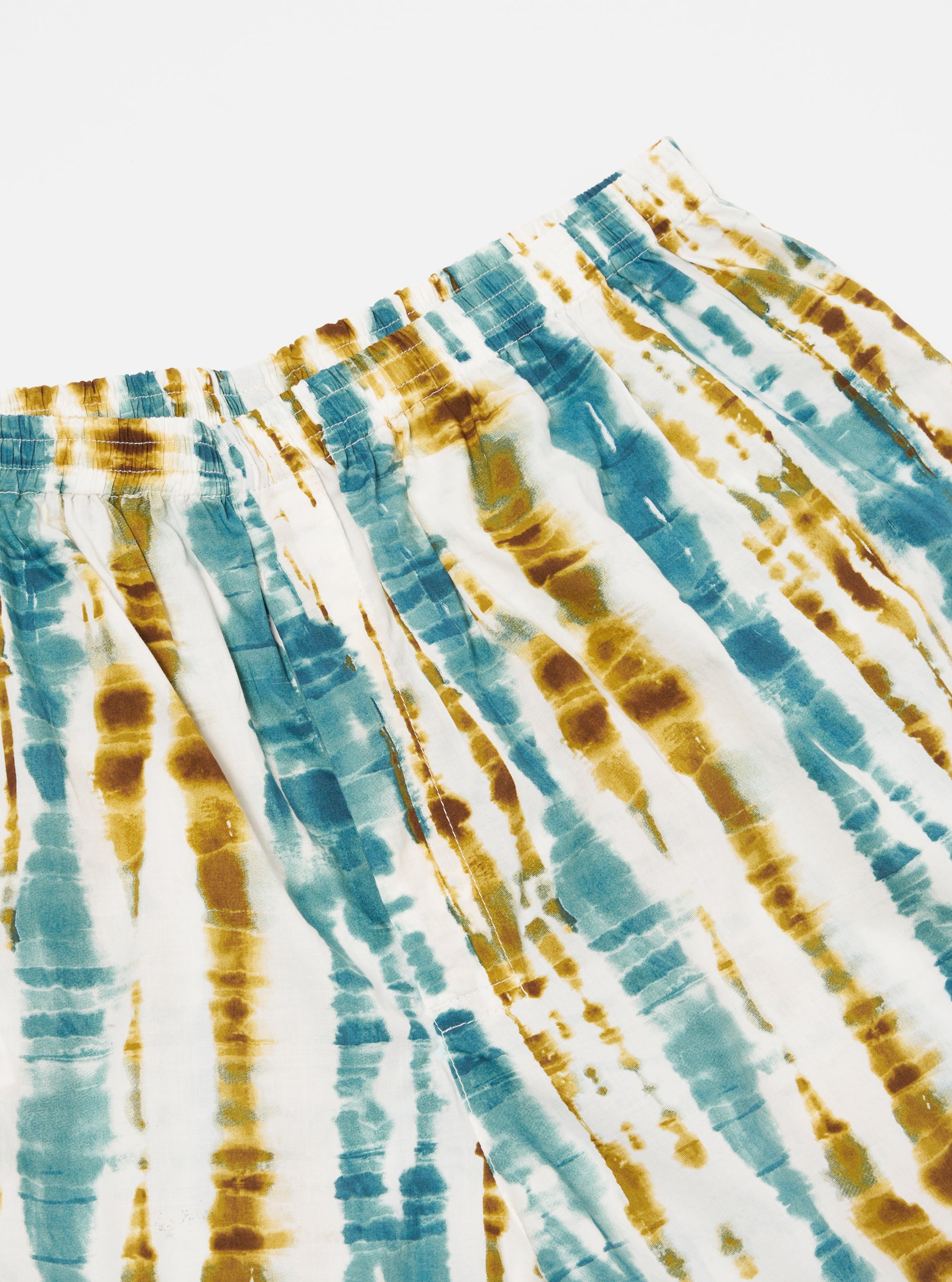 Close-up of the Ecru Paint Print Boxer Short on a white surface. The shorts feature a blue and brown tie-dye pattern with an elastic waistband.