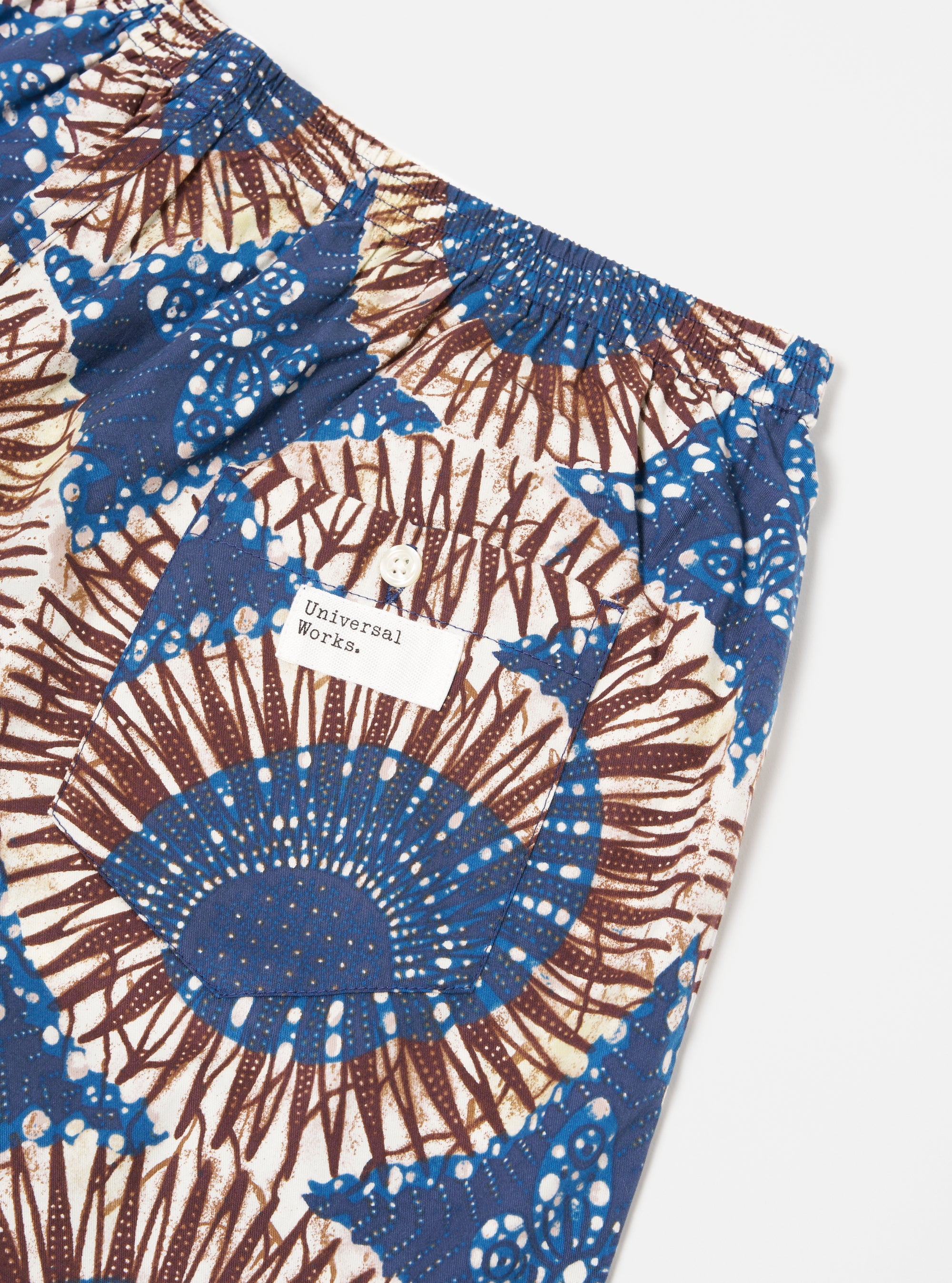 Close-up of the Navy Hokkoh Print Boxer Short on a white surface. The shorts feature a blue and brown pattern and a pocket with a 'Universal Works' label.