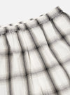 Close-up of the Ecru Shadow Check Pyjama Pant. The white and grey plaid fabric is gathered at the elastic waistband. Shot on a white background.