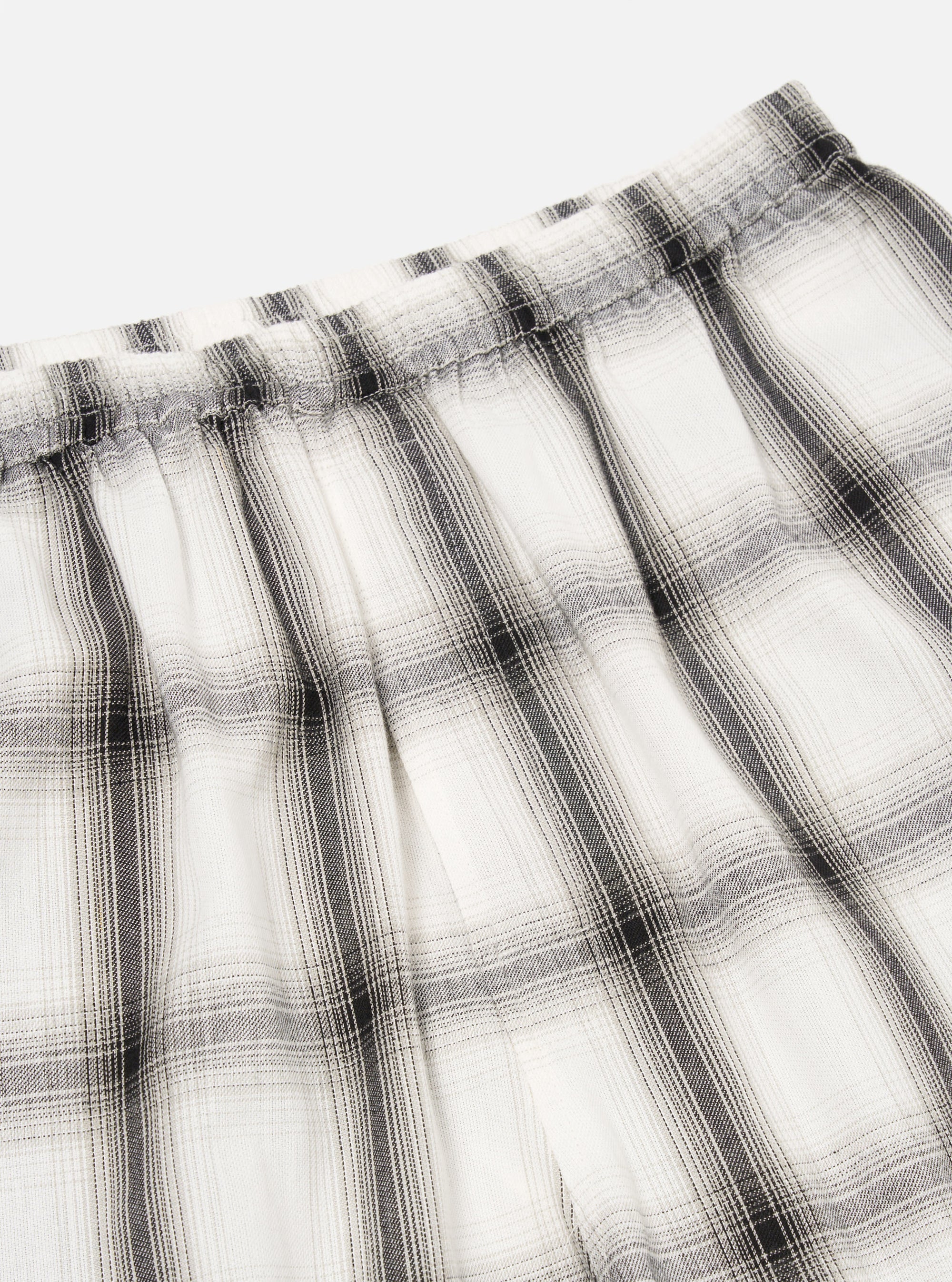 Close-up of the Ecru Shadow Check Pyjama Pant. The white and grey plaid fabric is gathered at the elastic waistband. Shot on a white background.