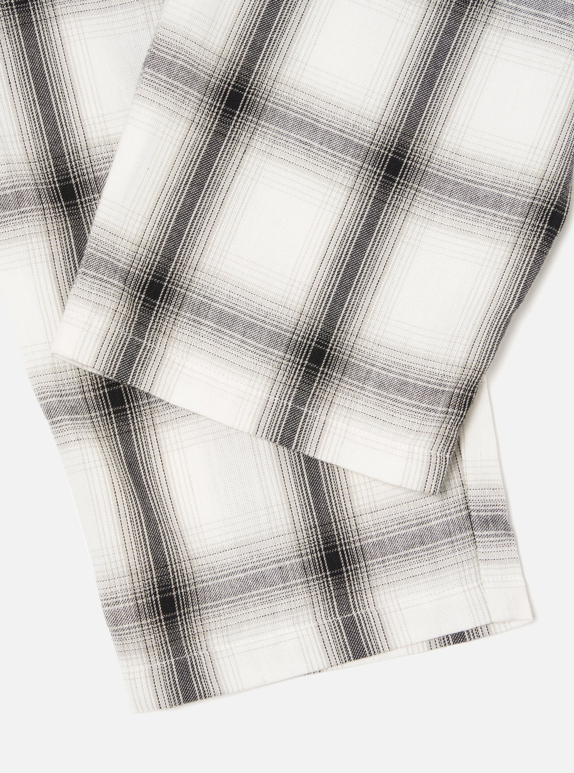 Close-up of the Ecru Shadow Check Pyjama Pant on a white surface. The fabric is a soft ecru with a subtle shadow check pattern in gray and black. The material looks soft and comfortable.
