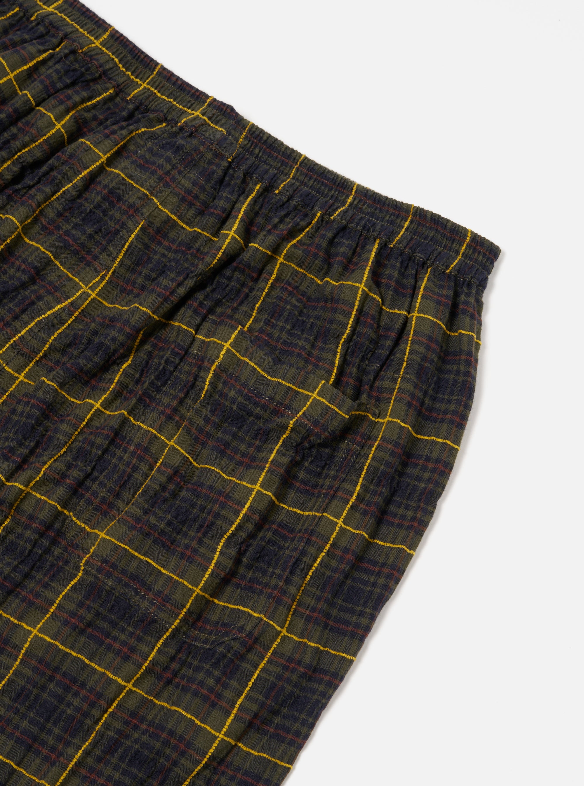 Close-up of Olive JP Herringbone Check Pyjama Pant on a white surface. The pant features a green, navy, and yellow plaid pattern with an elastic waistband.