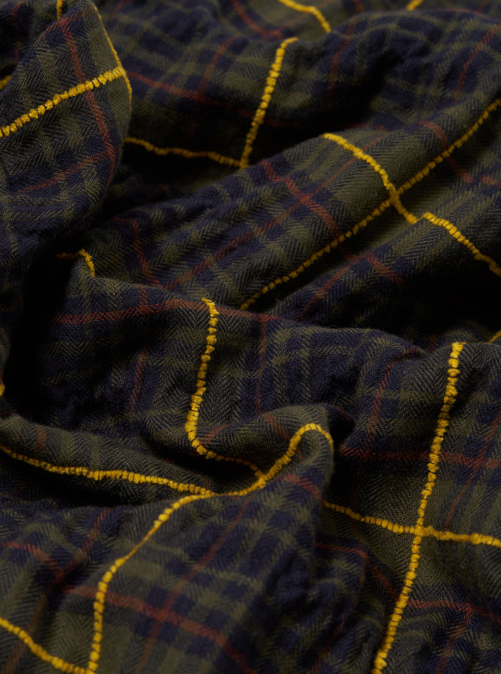 Close-up of the Olive JP Herringbone Check Pyjama Pant. Features a green, navy, red and yellow check pattern. The fabric is folded on a plain surface.