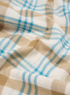 Close-up of the Ecru Madras Check Pyjama Pant fabric. Features a soft, brushed texture with ecru, tan, and blue checks. The fabric is draped to show its flow.