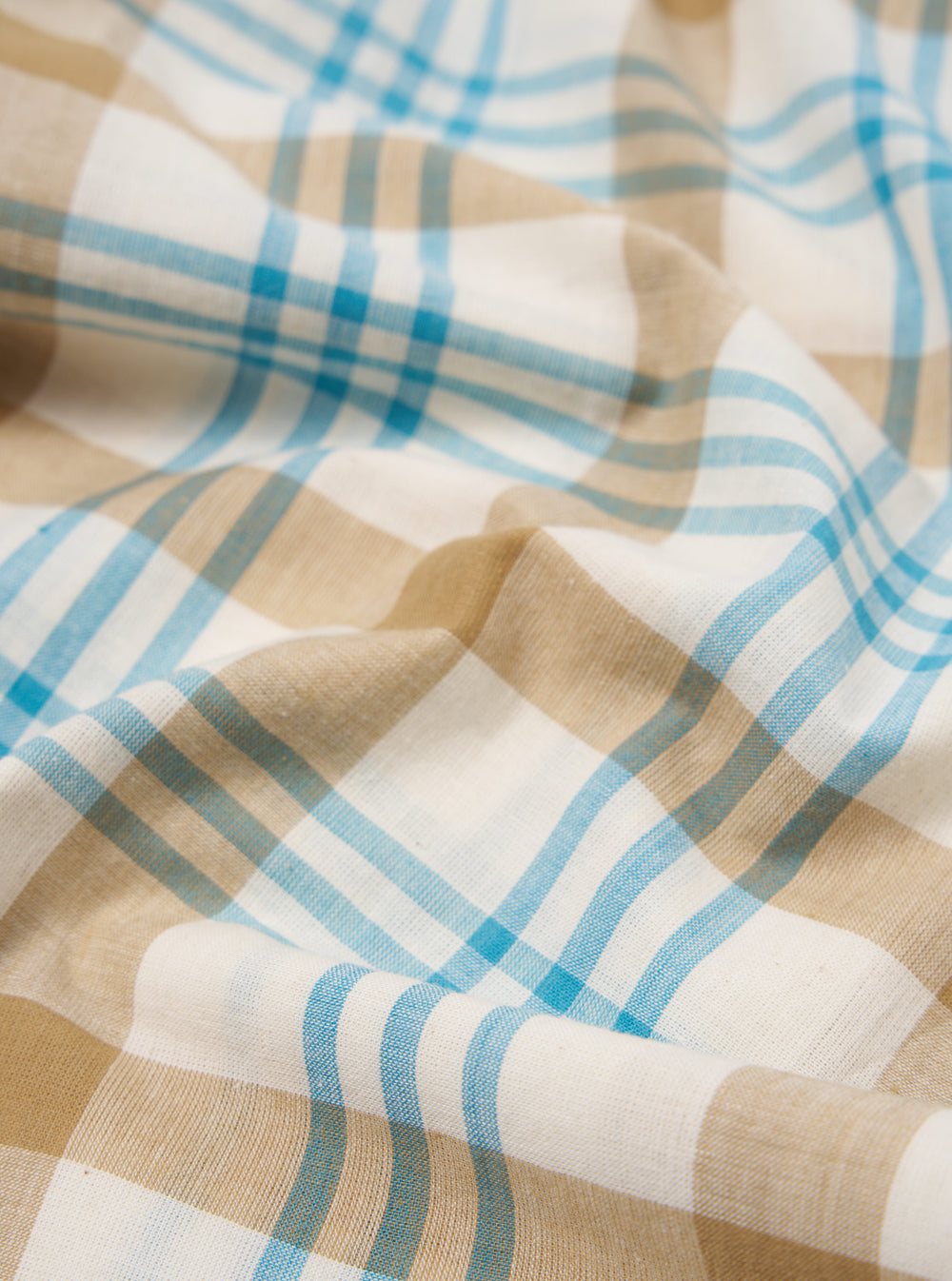 Close-up of the Ecru Madras Check Pyjama Pant fabric. Features a soft, brushed texture with ecru, tan, and blue checks. The fabric is draped to show its flow.