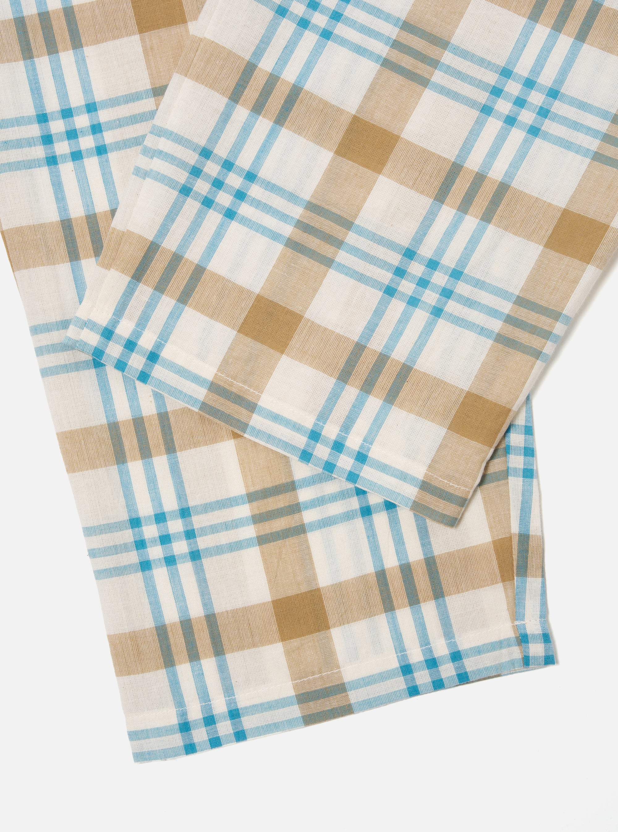 Close-up of the Ecru Madras Check Pyjama Pant on a white surface. The cotton fabric features a blue, tan, and white plaid pattern.