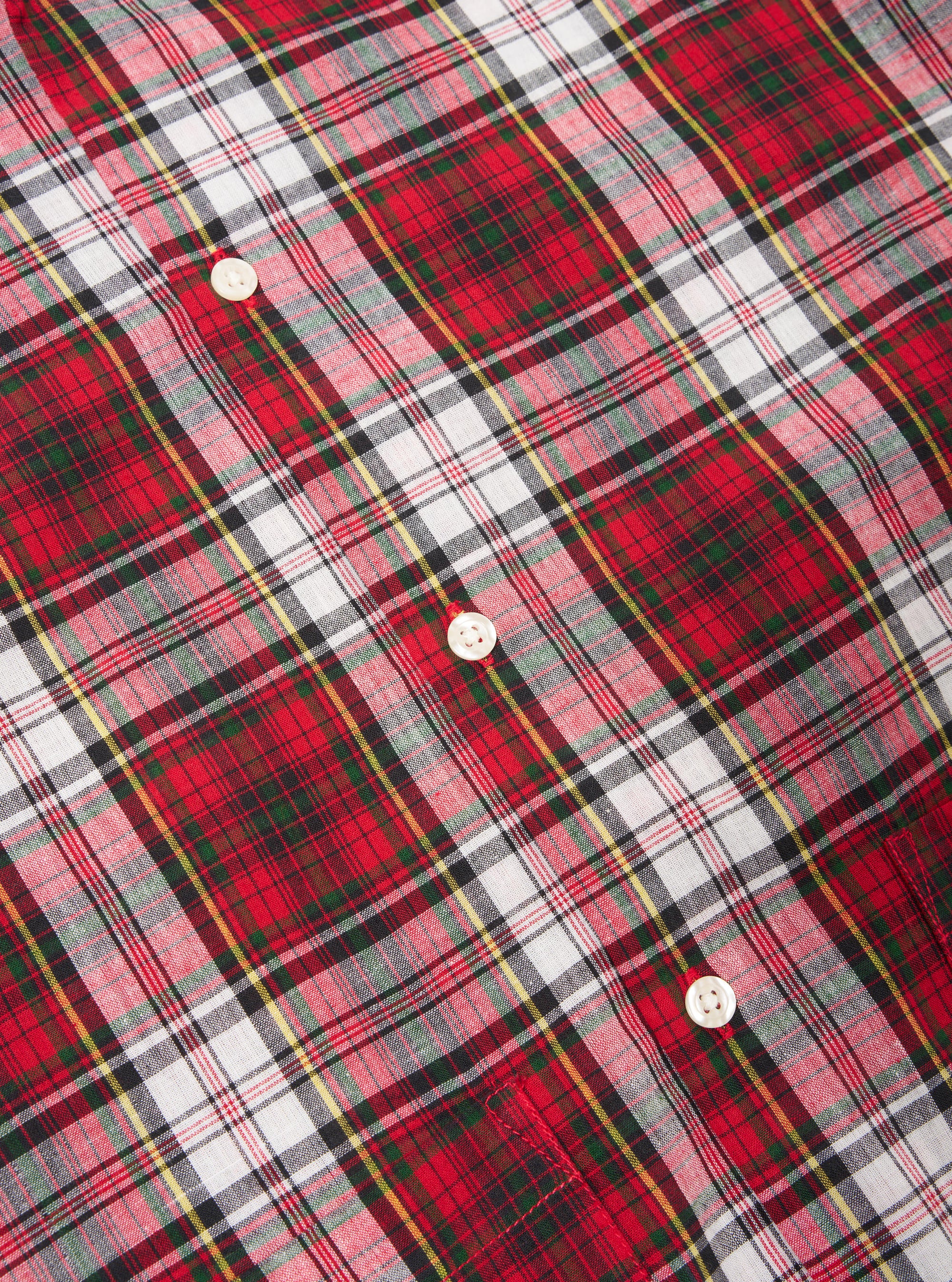 Close-up of the Red Madras Check Short Pyjama Set. Features a red, white, green, and black plaid pattern with white buttons. The fabric is neatly arranged on a flat surface.